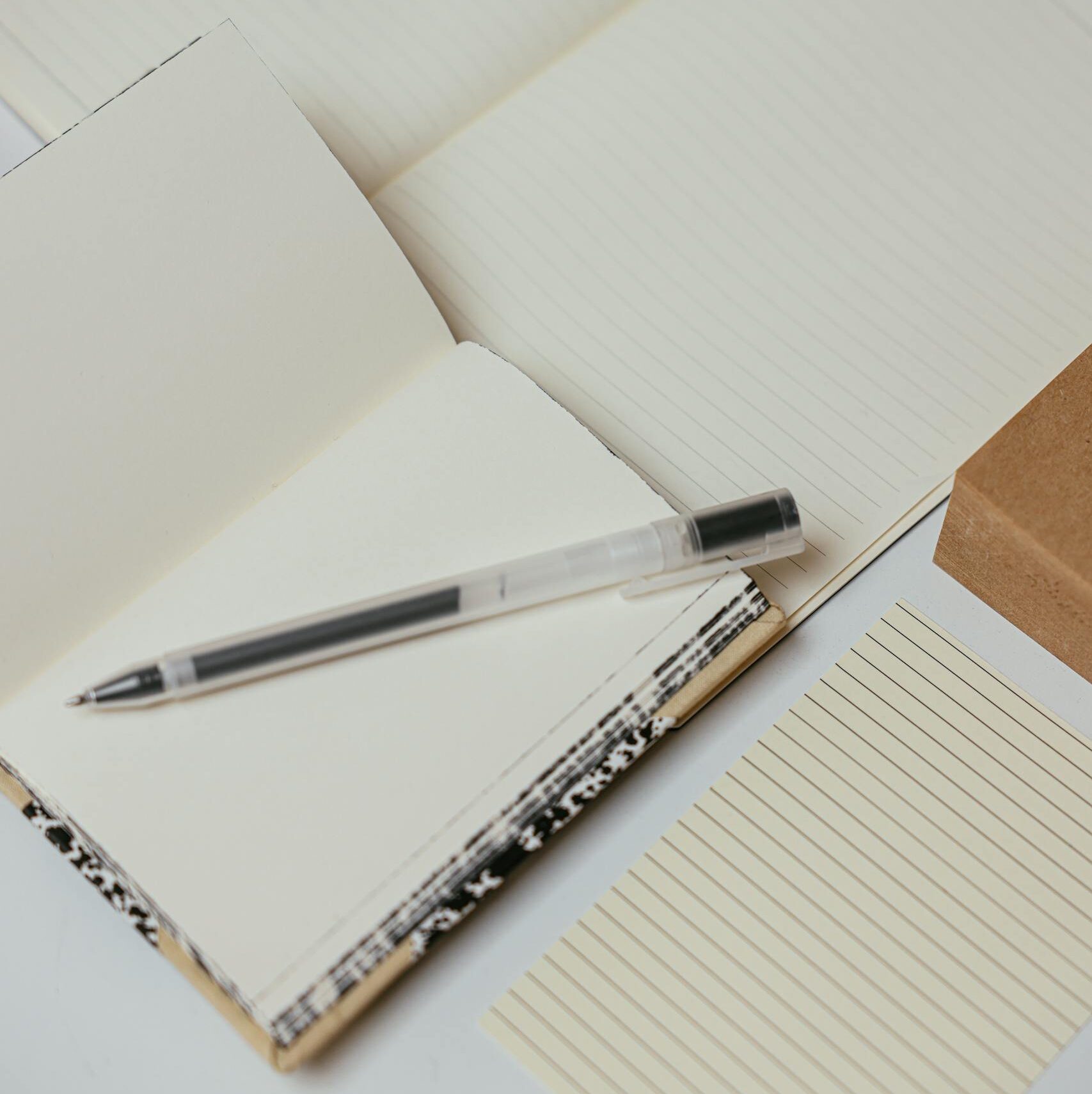 A flat lay of notebooks, pens, and stationery on a clean, minimalist desk surface.