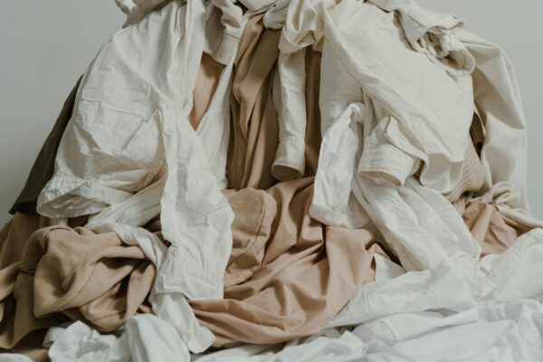 A heap of beige and white clothes casually piled on a wooden floor.