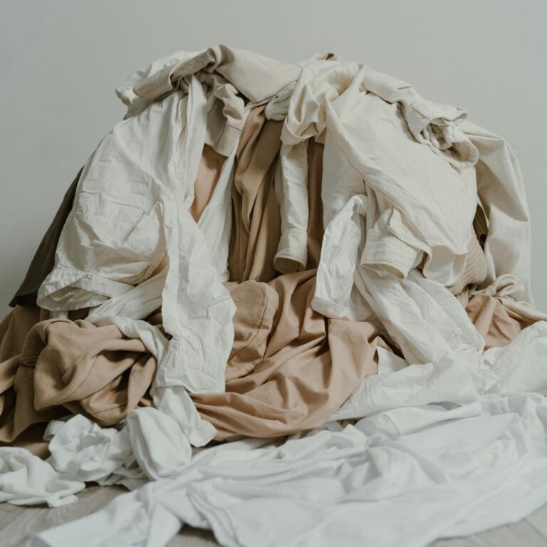 A heap of beige and white clothes casually piled on a wooden floor.