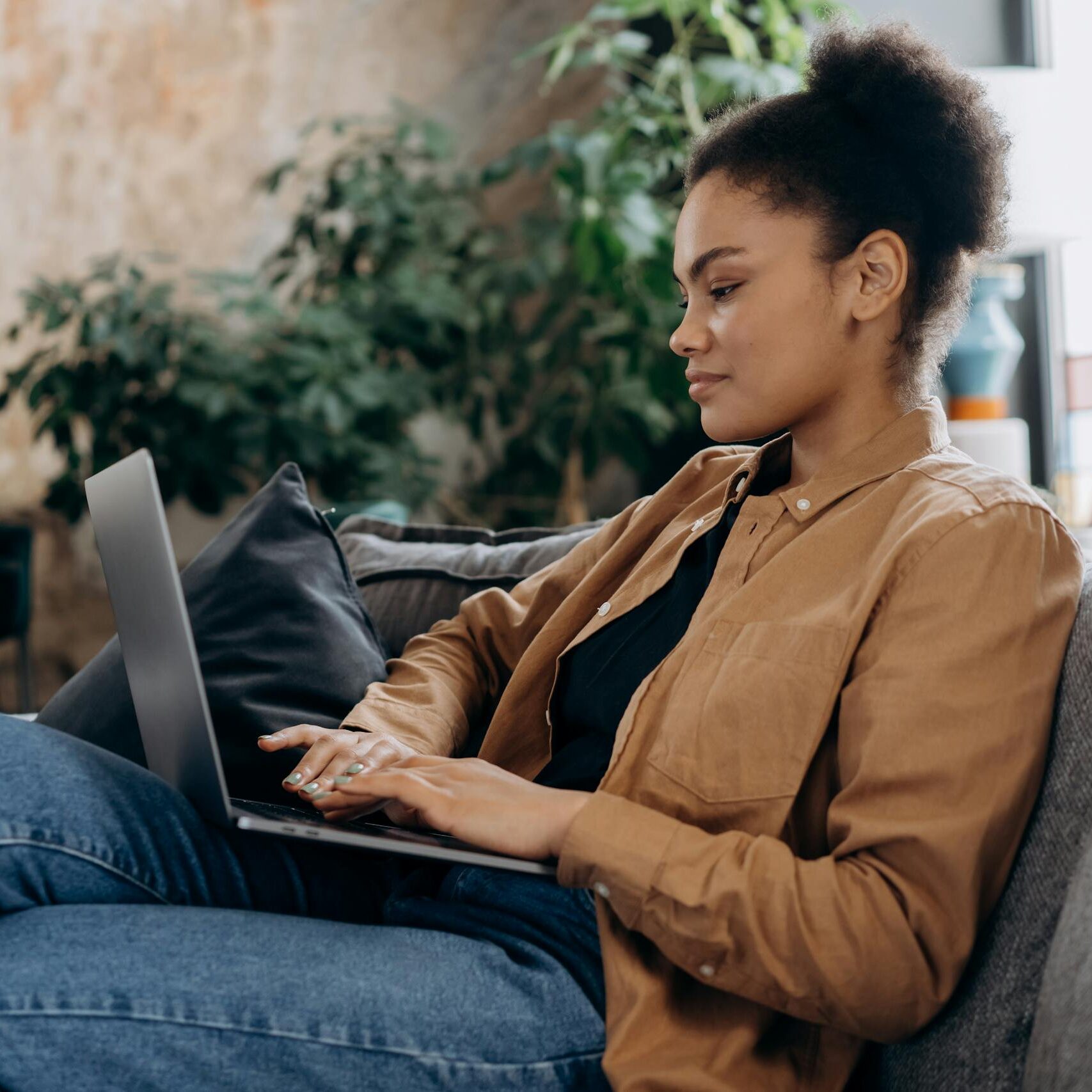 A young woman in casual clothing works on her laptop in a cozy home office setting.