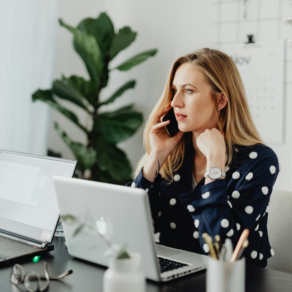 Businesswoman multitasking with phone and laptop in a modern office environment.