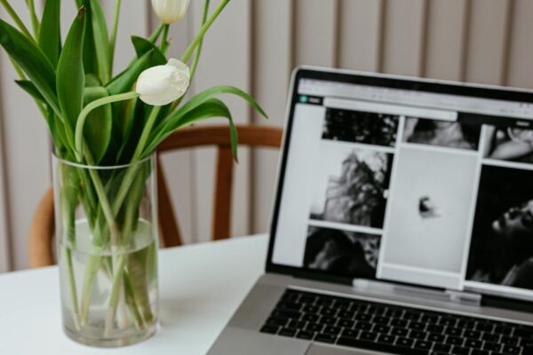 Cozy workspace featuring a laptop, pencil, notepad, and a vase of blooming white tulips on a modern desk.