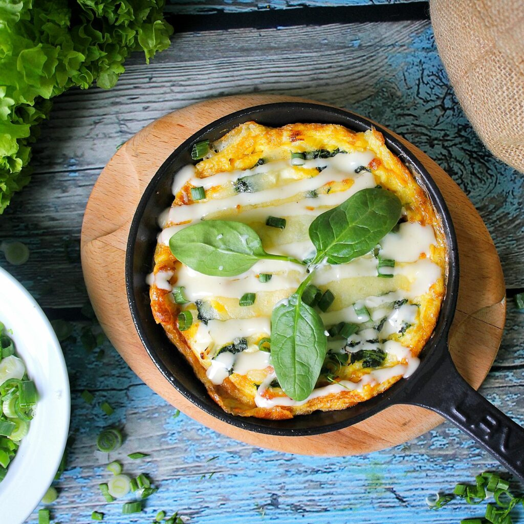 Delicious gourmet omelette with melted cheese and green onions in a skillet, garnished with fresh lettuce.