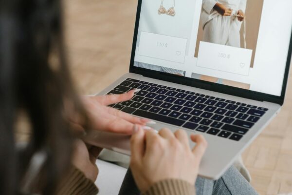 Female browsing an online fashion store on a laptop indoors, focusing on clothing and accessories.