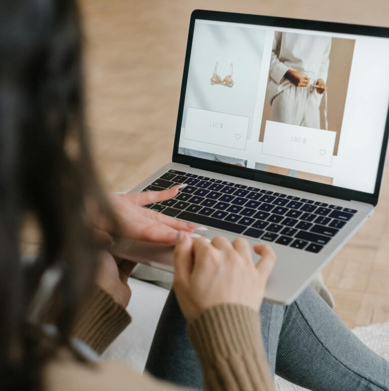 Female browsing an online fashion store on a laptop indoors, focusing on clothing and accessories.