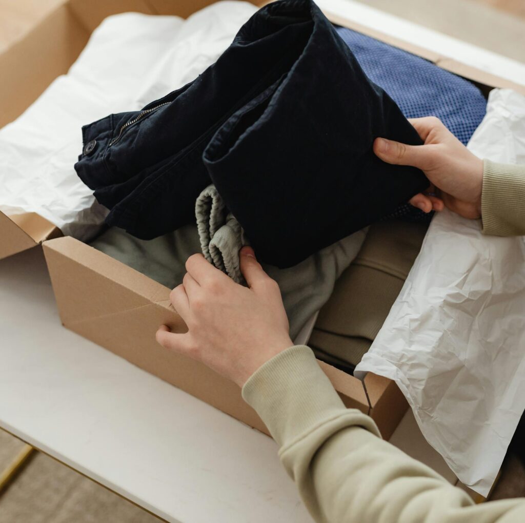 Person unpacking clothes from a delivery box indoors, showcasing a range of garments.