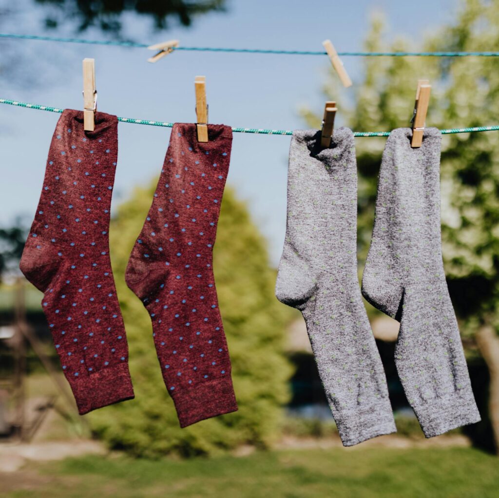 Soft focus of washed multicolored socks hanging on rope with clothespins outdoors on sunny summer day against natural background
