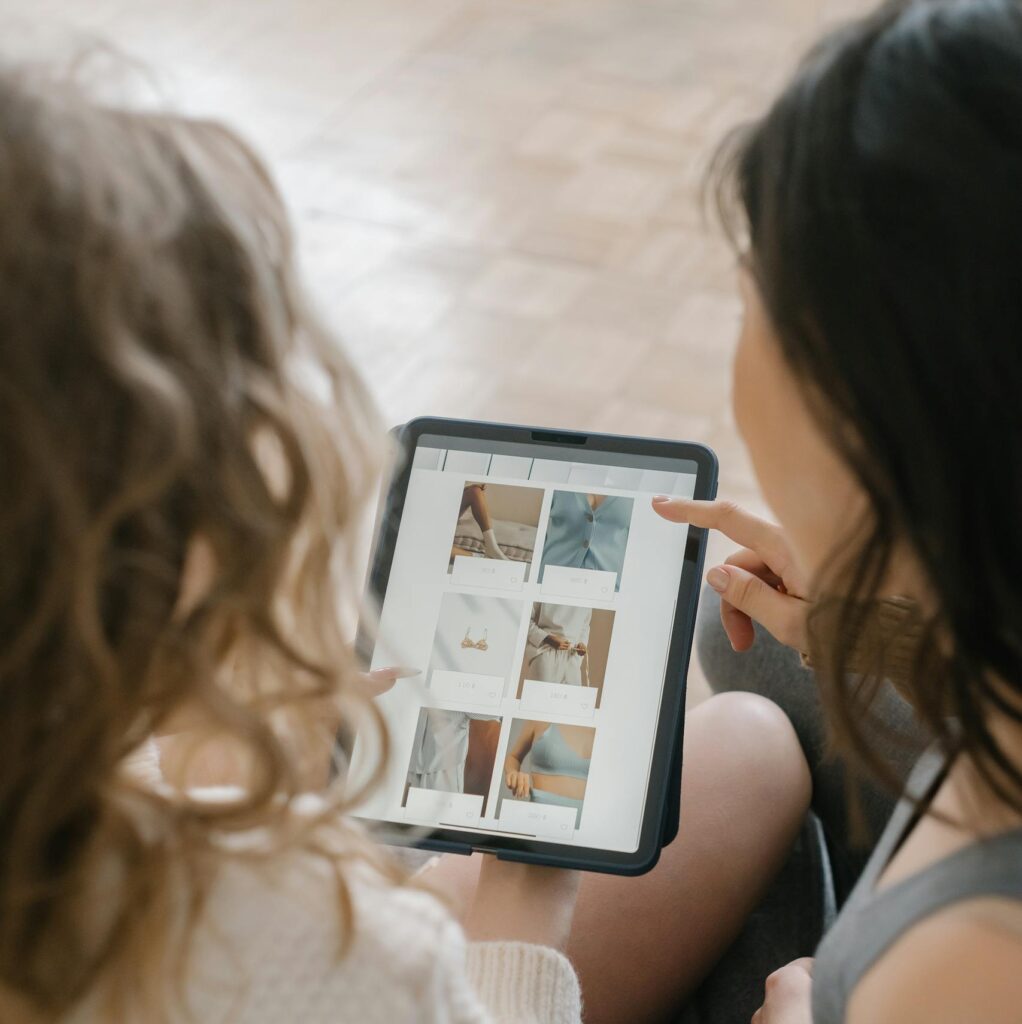 Two women sitting together, shopping online using a tablet, sharing ideas and browsing products.