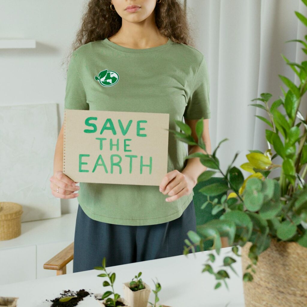 Young woman promoting eco-awareness with a 'Save The Earth' sign indoors.