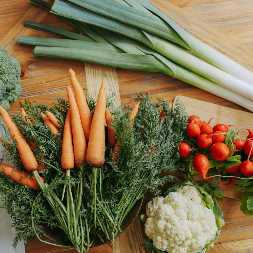 A colorful assortment of fresh vegetables including carrots, leeks, and radishes displayed on a wooden table.