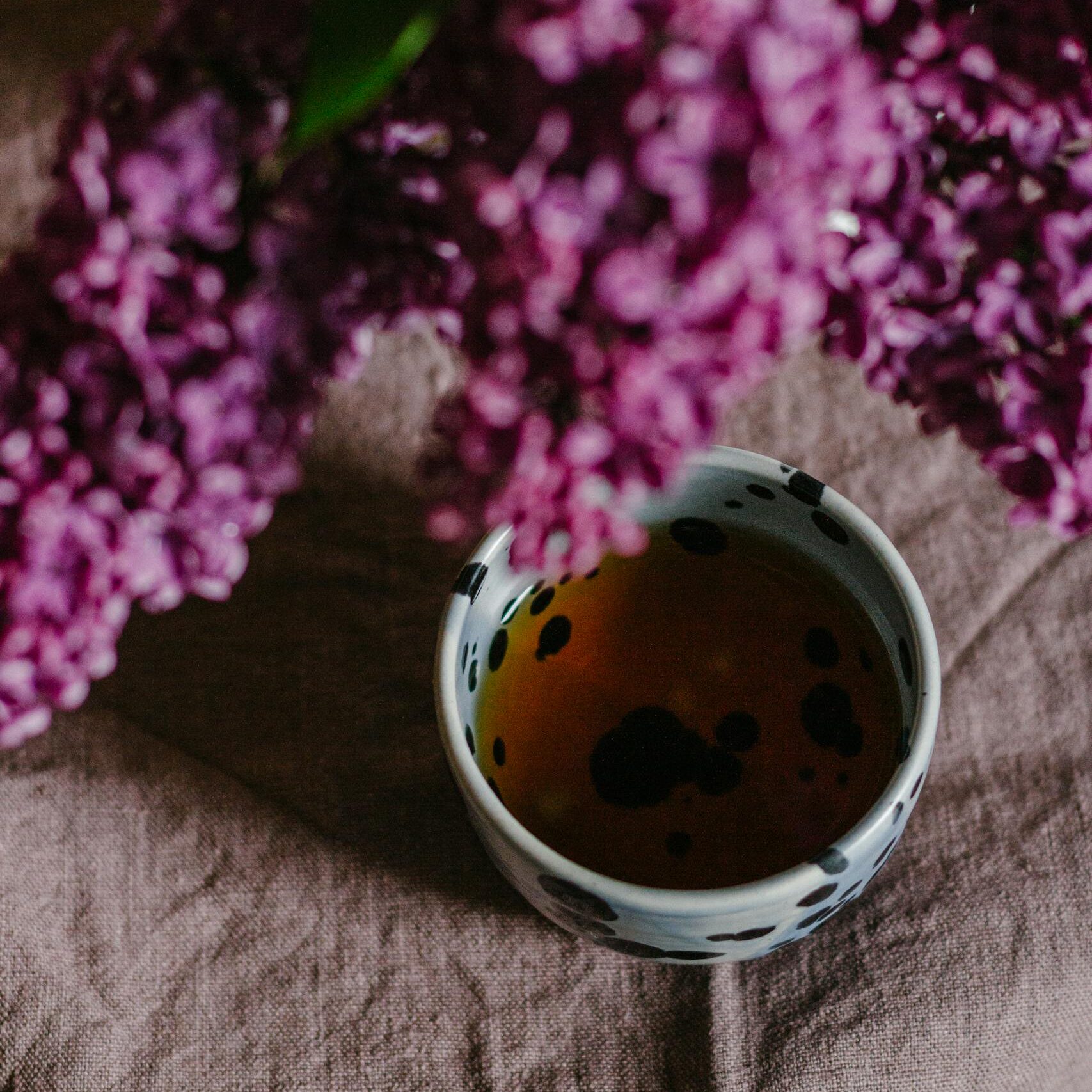 A cozy composition featuring purple lilacs above a steaming cup of tea.