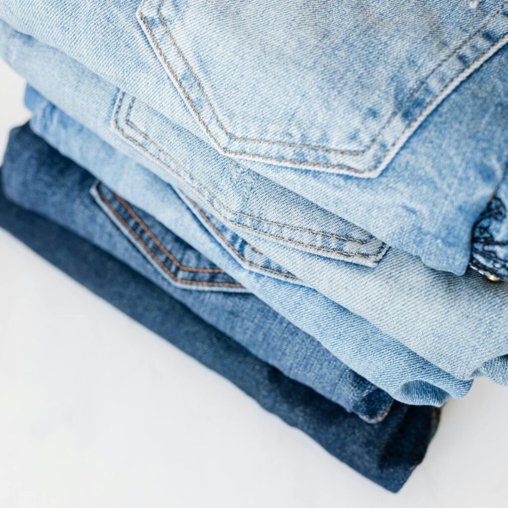 A neatly stacked pile of blue denim jeans showcasing various shades and styles in a minimalist setting.