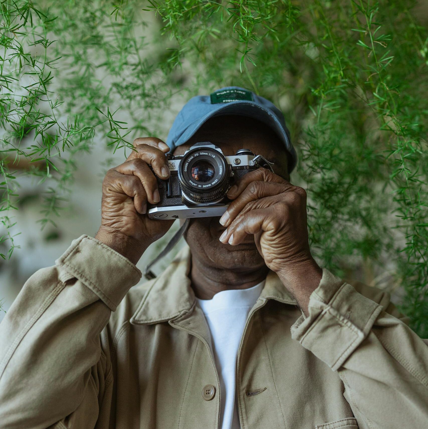 An adult holding a vintage camera amidst lush green foliage, capturing moments with passion.