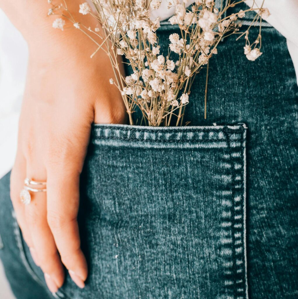 Close-up of a hand with wildflowers in the back pocket of blue jeans, emphasizing a feminine and casual style.