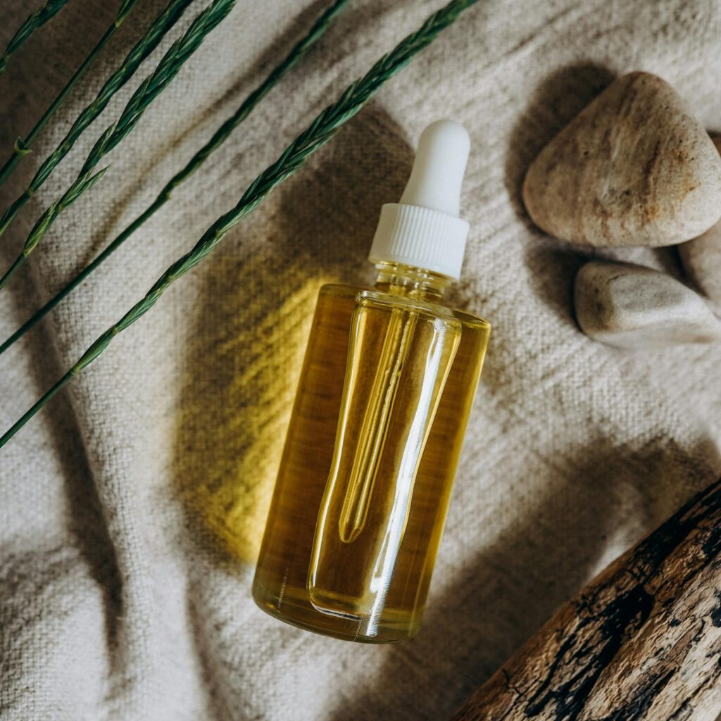 Elevated view of natural skincare serum bottle on fabric with stones and wood elements.