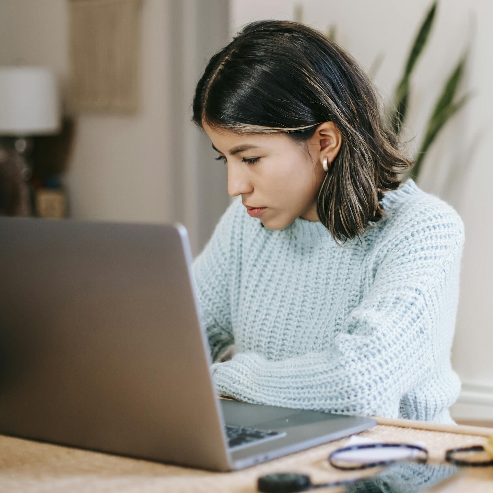 Focused young woman using laptop at home while drinking coffee. Ideal for remote work and study themes.