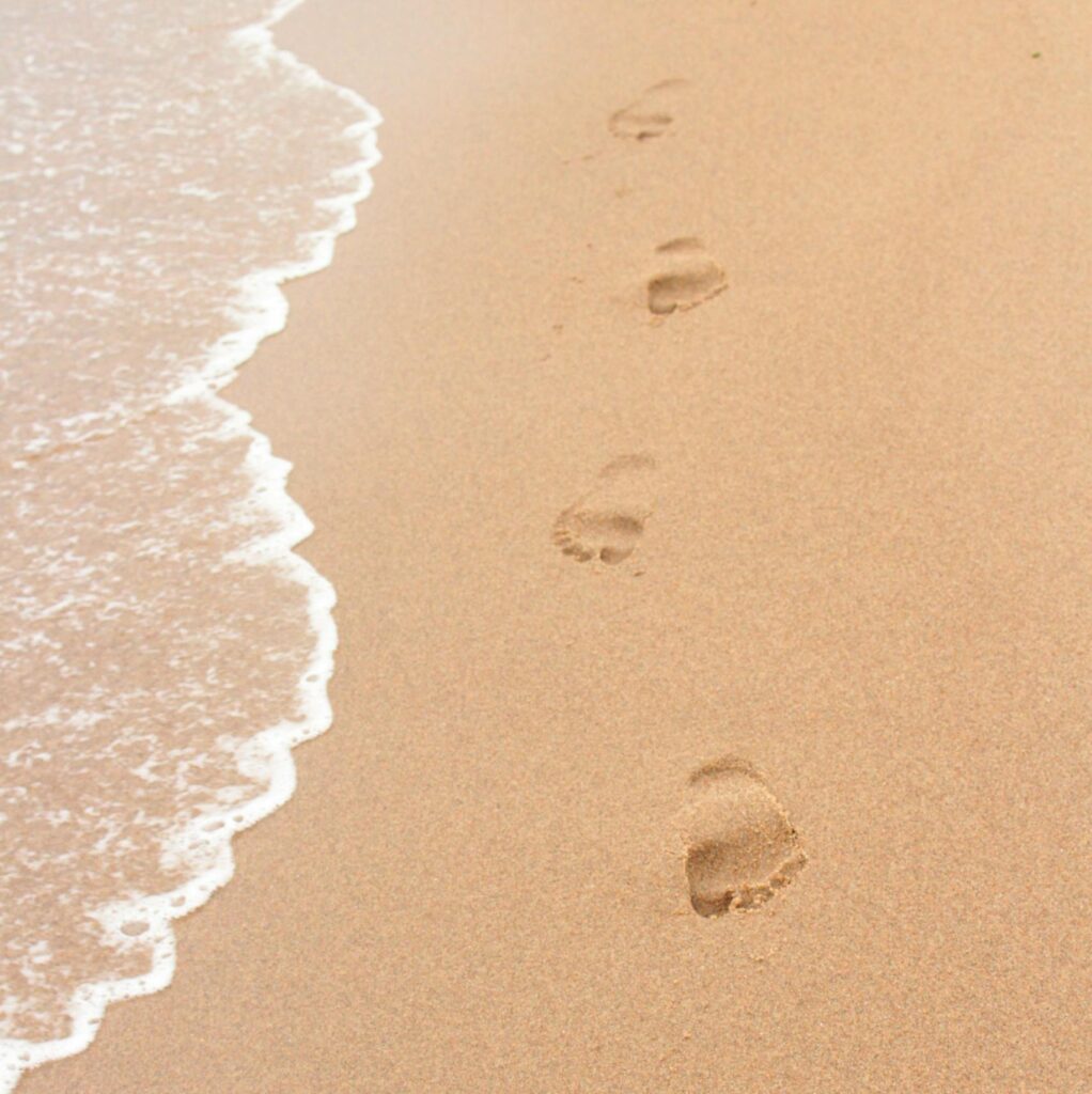 Footprints on a sandy beach beside ocean waves, perfect for summer themes.