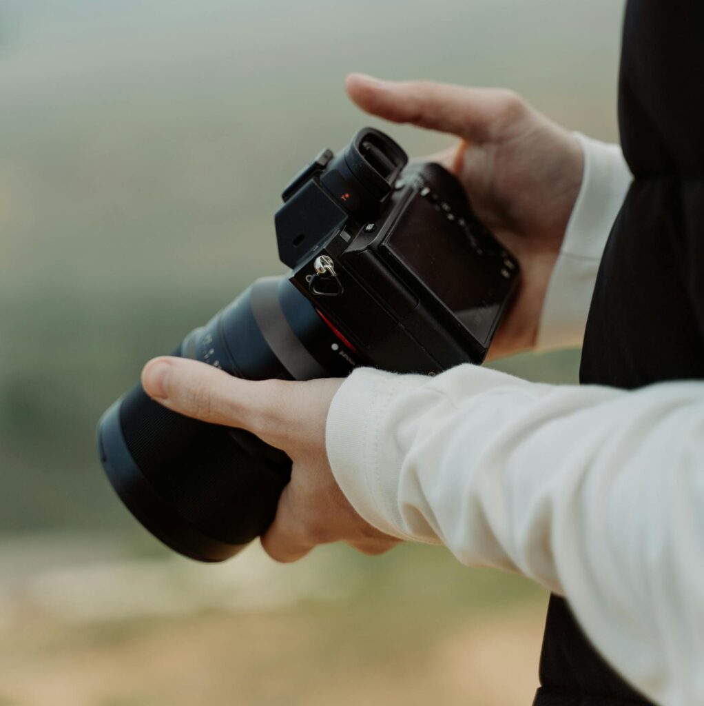 Hands holding a DSLR camera outdoors with a blurred background. Perfect for photography themes.