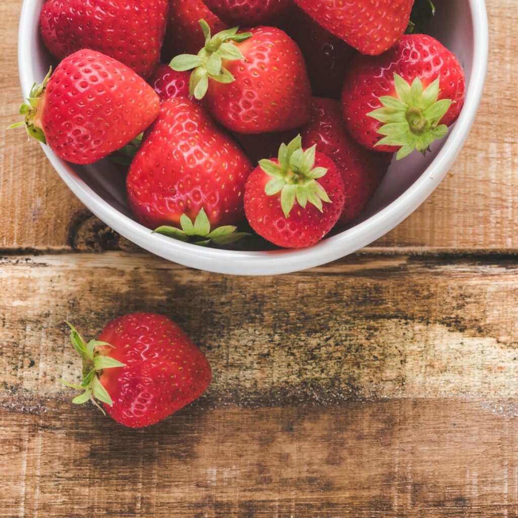 Juicy red strawberries in a white bowl on a wooden table, showcasing freshness.