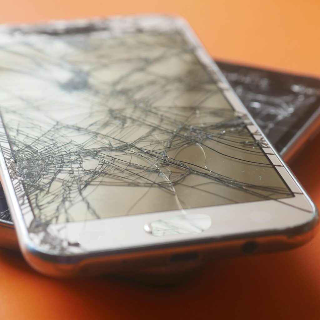 Two broken smartphone screens on an orange background, illustrating device fragility.
