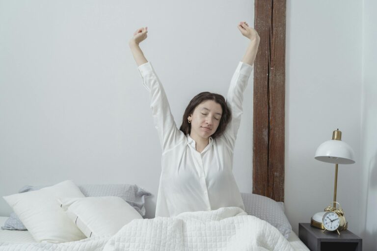 Woman with closed eyes stretching in bed at home during a peaceful morning.