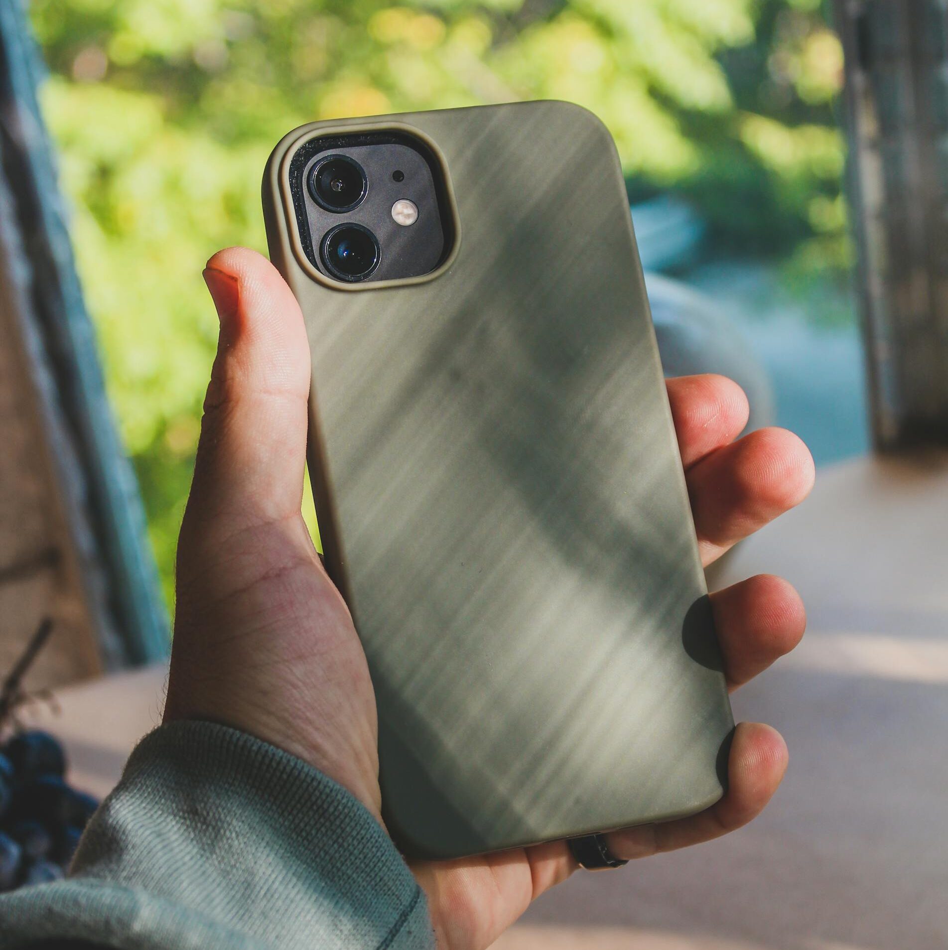 A hand holding a green smartphone case near a window with natural light.