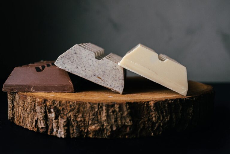 Assorted delicious sweet chocolate bars served on wooden tray against blurred gray background in studio