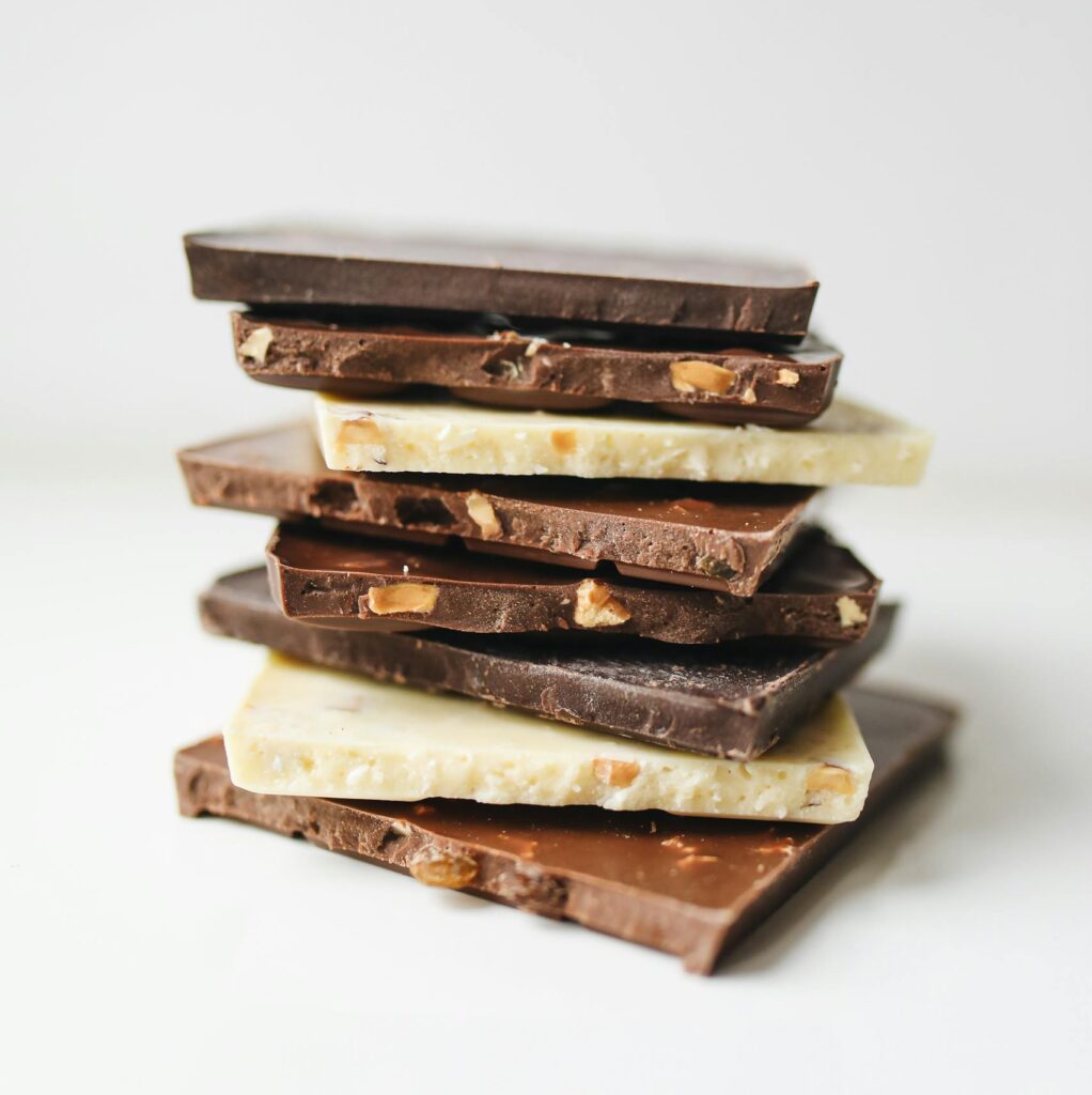 Assorted stacked chocolate bars featuring white, milk, and dark varieties with nut inclusions.