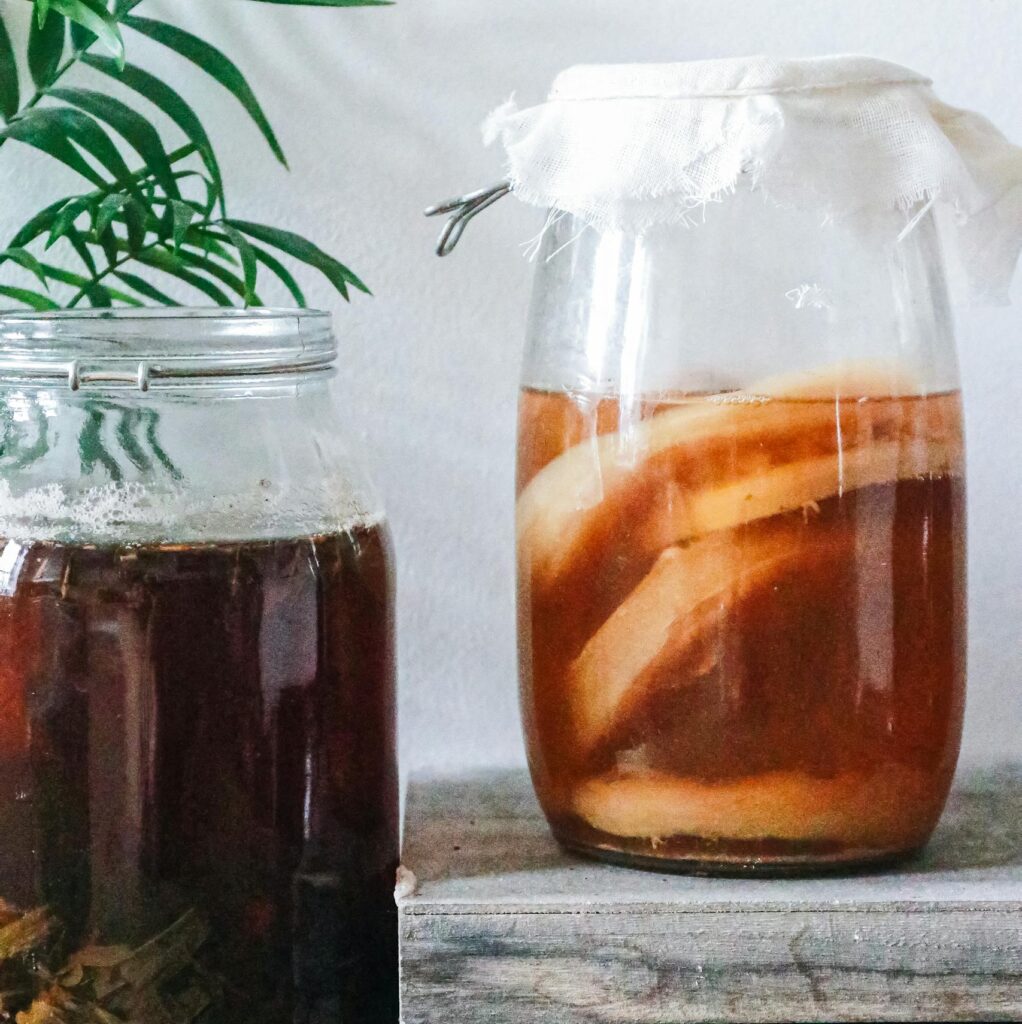 Close-up of kombucha brewing in jars with a rustic setting, showcasing natural fermentation process.