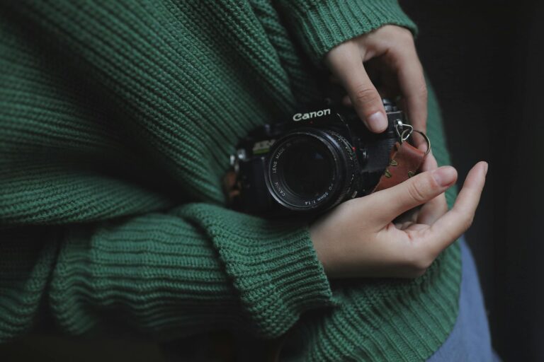 Close-up shot of hands holding a vintage camera with a green knitted sweater.