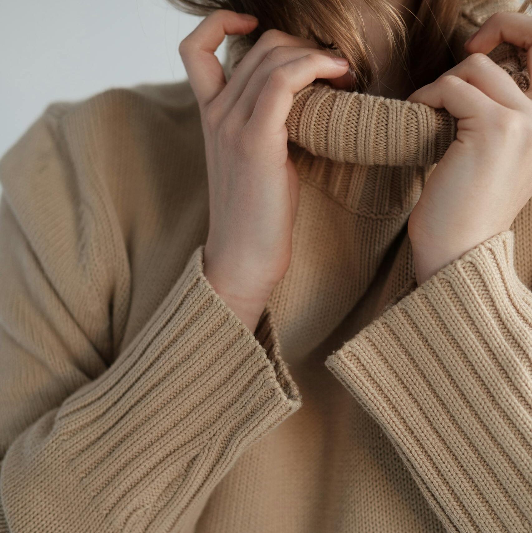 Crop unrecognizable female with long hair wearing soft warm sweater with long collar