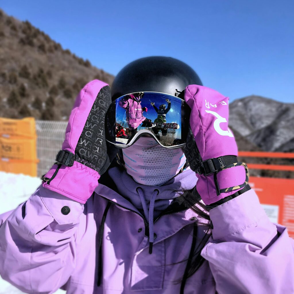 A person dressed for skiing or snowboarding in winter gear, capturing a mountain scene reflected in goggles.