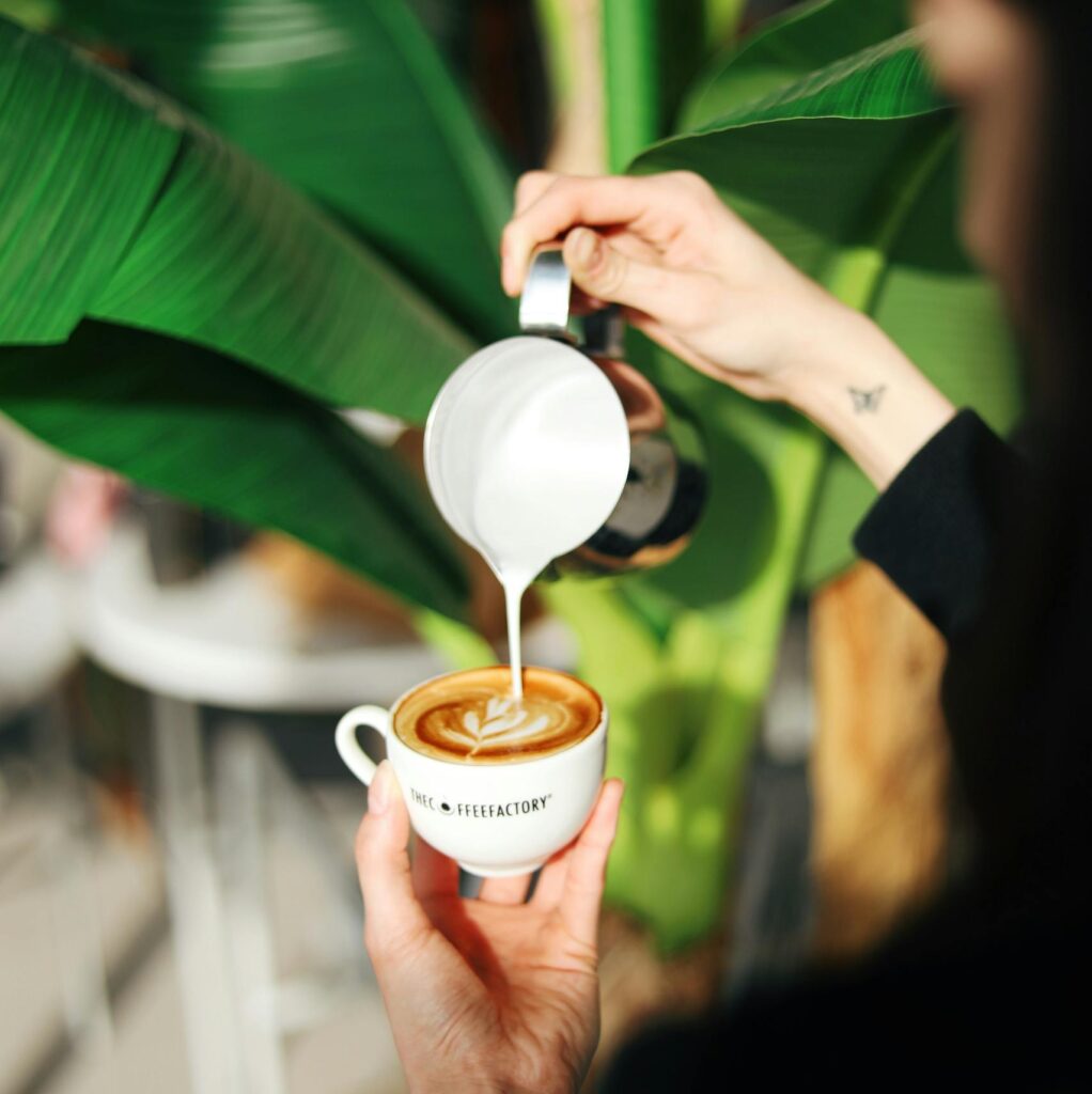 Close-up of latte art being crafted with a green plant backdrop.