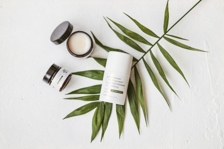Minimalist product shot of CBD ointment and leaf on white background.
