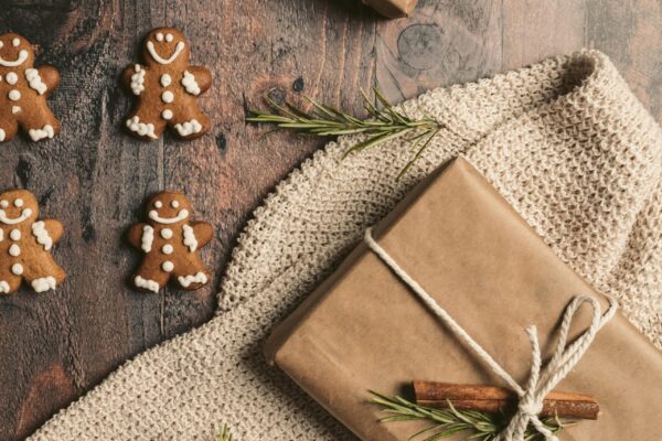 Top view of gingerbread men and wrapped gift with holiday decorations on wooden table.