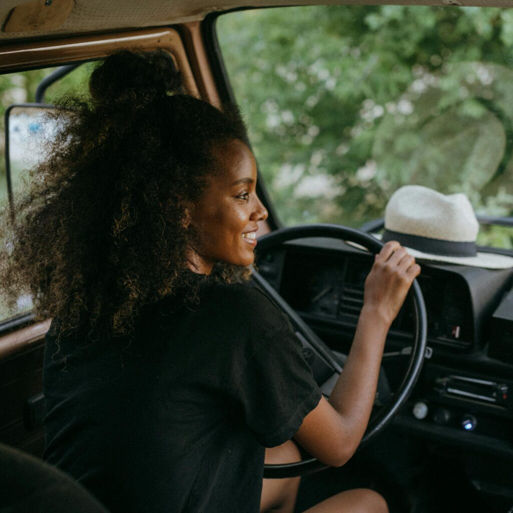 Woman driving a van through nature, enjoying a summer road trip journey.