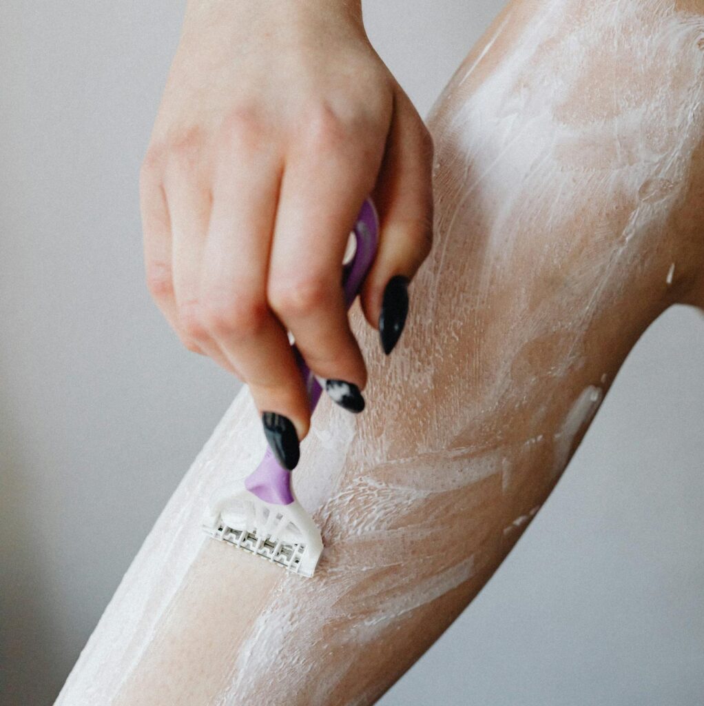 Close-up of a woman's hand using a razor to shave her legs with foam, depicting personal care.