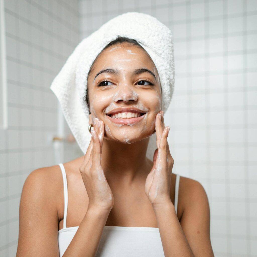 Smiling woman with face wash in a bathroom, embracing self-care and fresh skin.
