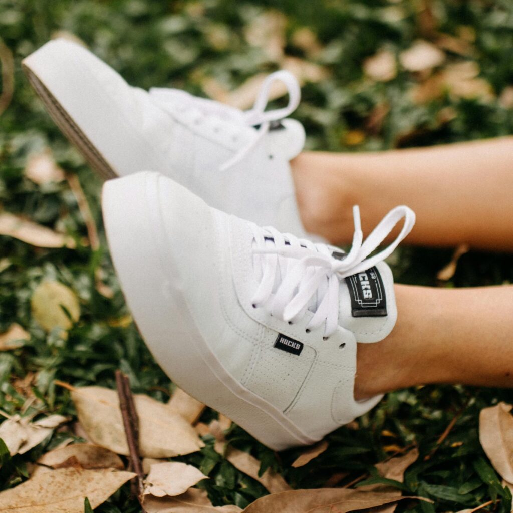 Stylish white sneakers on leafy ground, perfect for nature-themed fashion.