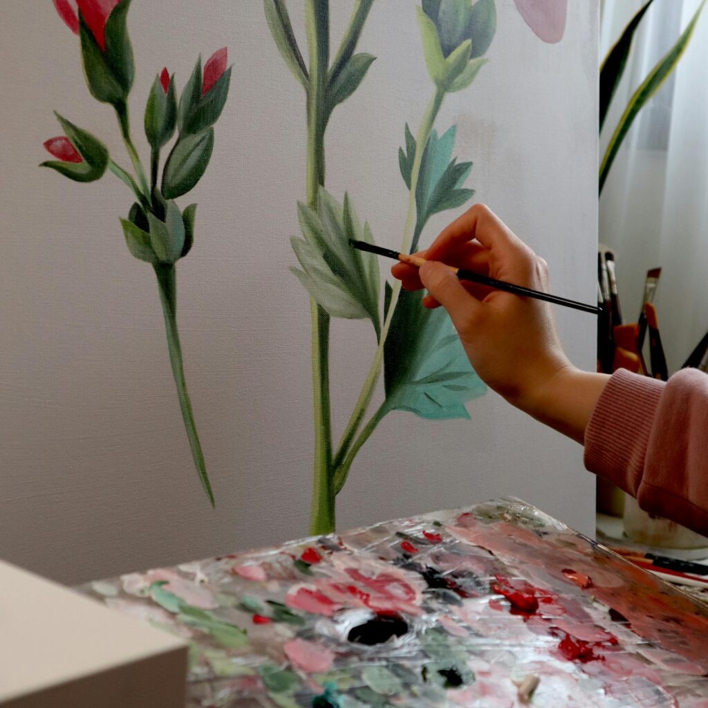 Artist painting flowers on canvas with palette, emphasizing creativity and artistry.