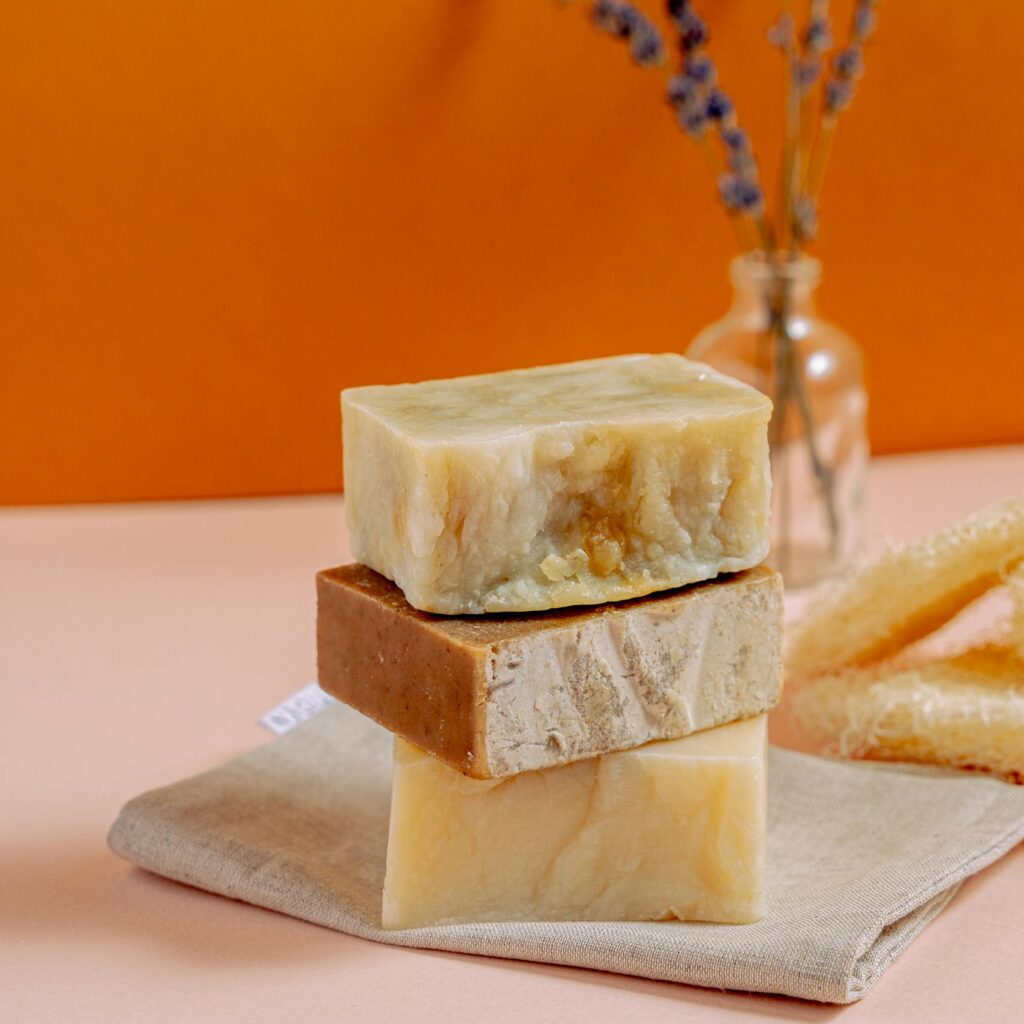 Three stacked natural handmade soap bars with lavender and honey on a pastel surface.