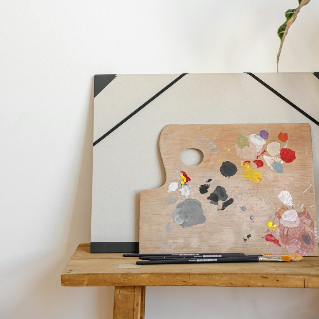 Wooden artist's palette with mixed paints on canvas, set against a plain wall.