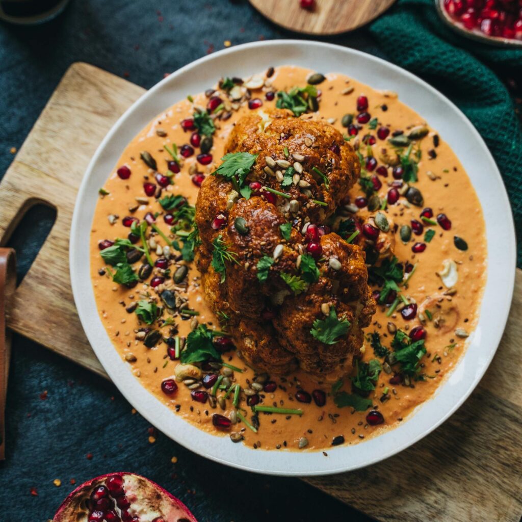 Delicious roasted cauliflower with vibrant garnet sauce and garnished with herbs, perfect for a healthy vegan meal.