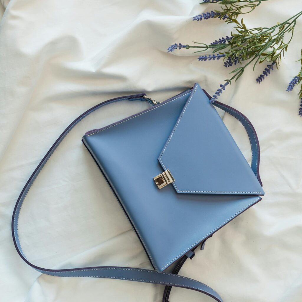 Stylish blue leather purse against a white background with lavender accents, perfect for chic fashion.