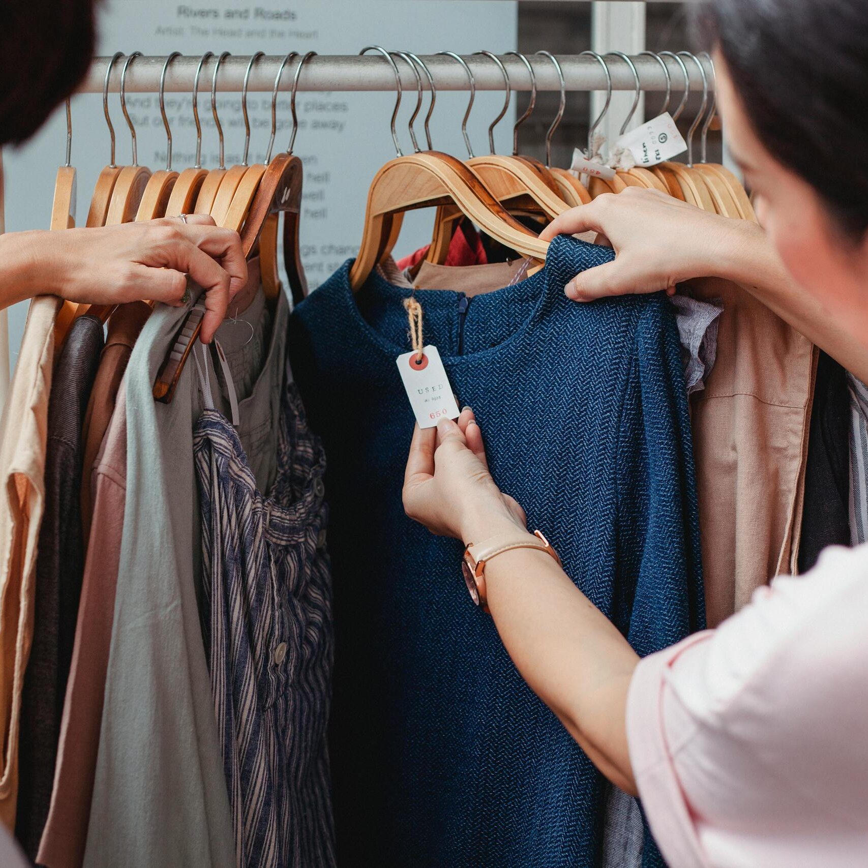 Two women browse clothes in a boutique, examining a blue dress.