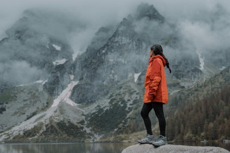 Woman in orange jacket hiking through foggy mountain landscape, admiring the view.