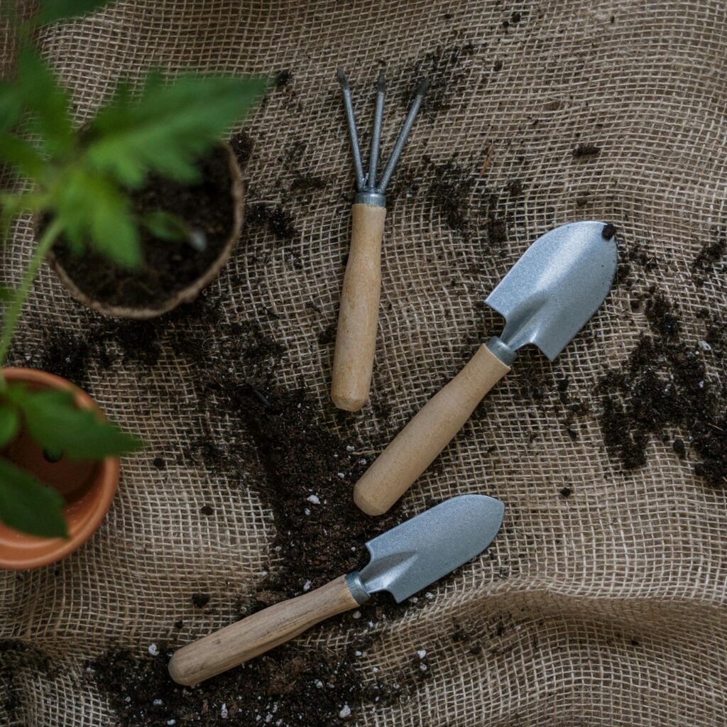 Gardening tools with potted plants and soil on burlap, perfect for home gardening themes.