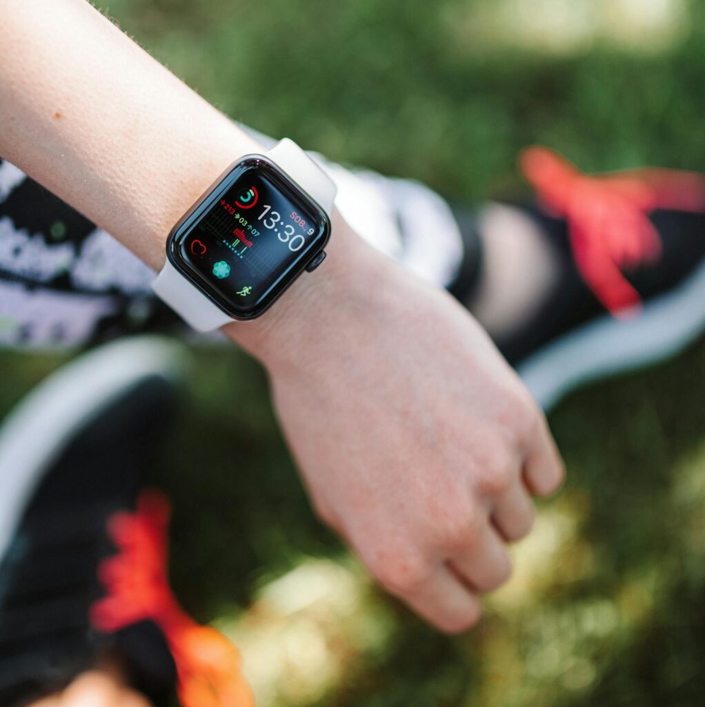 A smartwatch displaying time and apps on a person's wrist outdoors, with sporty shoes visible.
