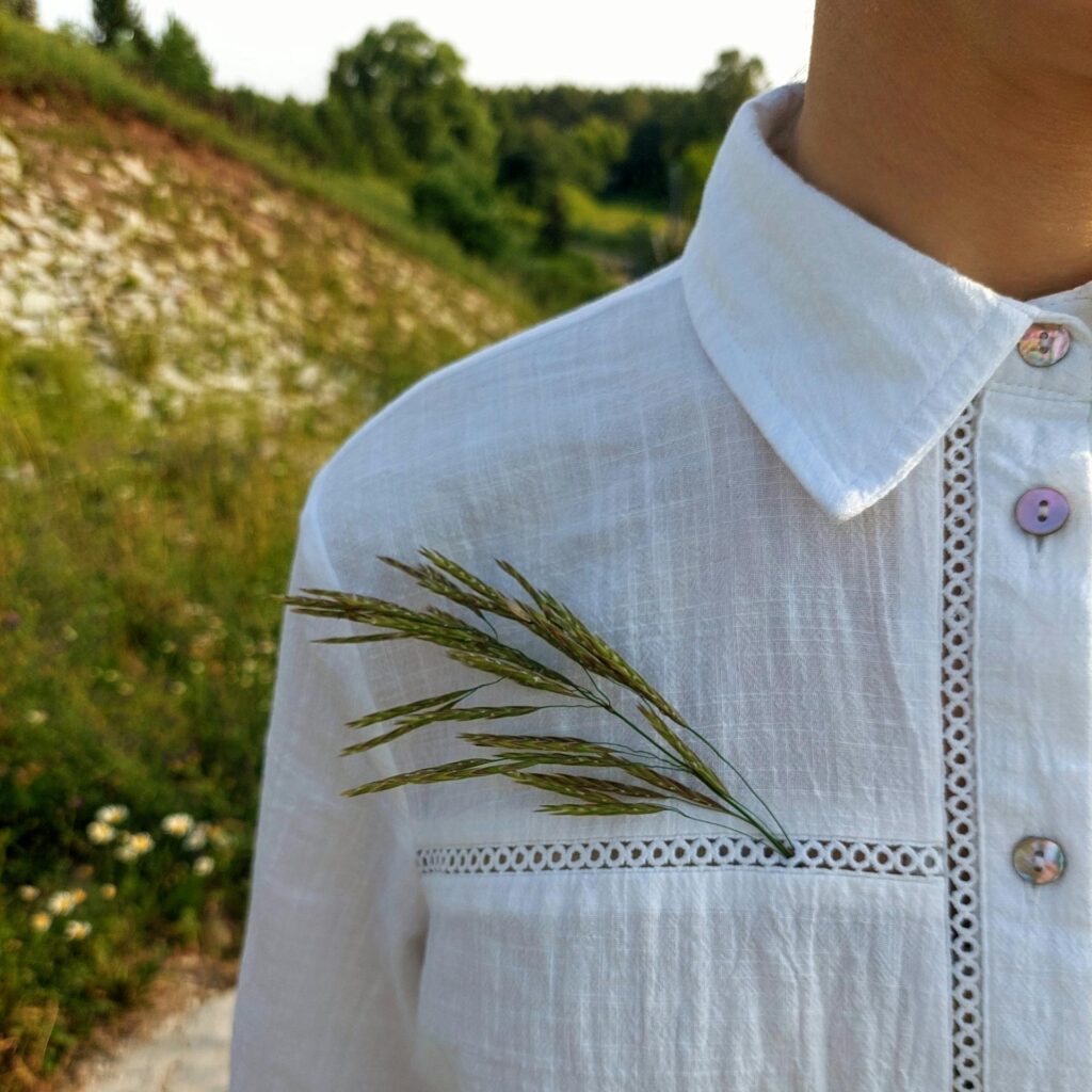 Close-up of a woman in a white shirt with grass tucked in, outdoors in a lush green field.