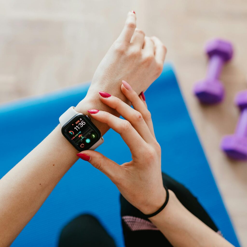 Unrecognizable female in sportswear sitting on blue yoga mat on floor and checking smart watch